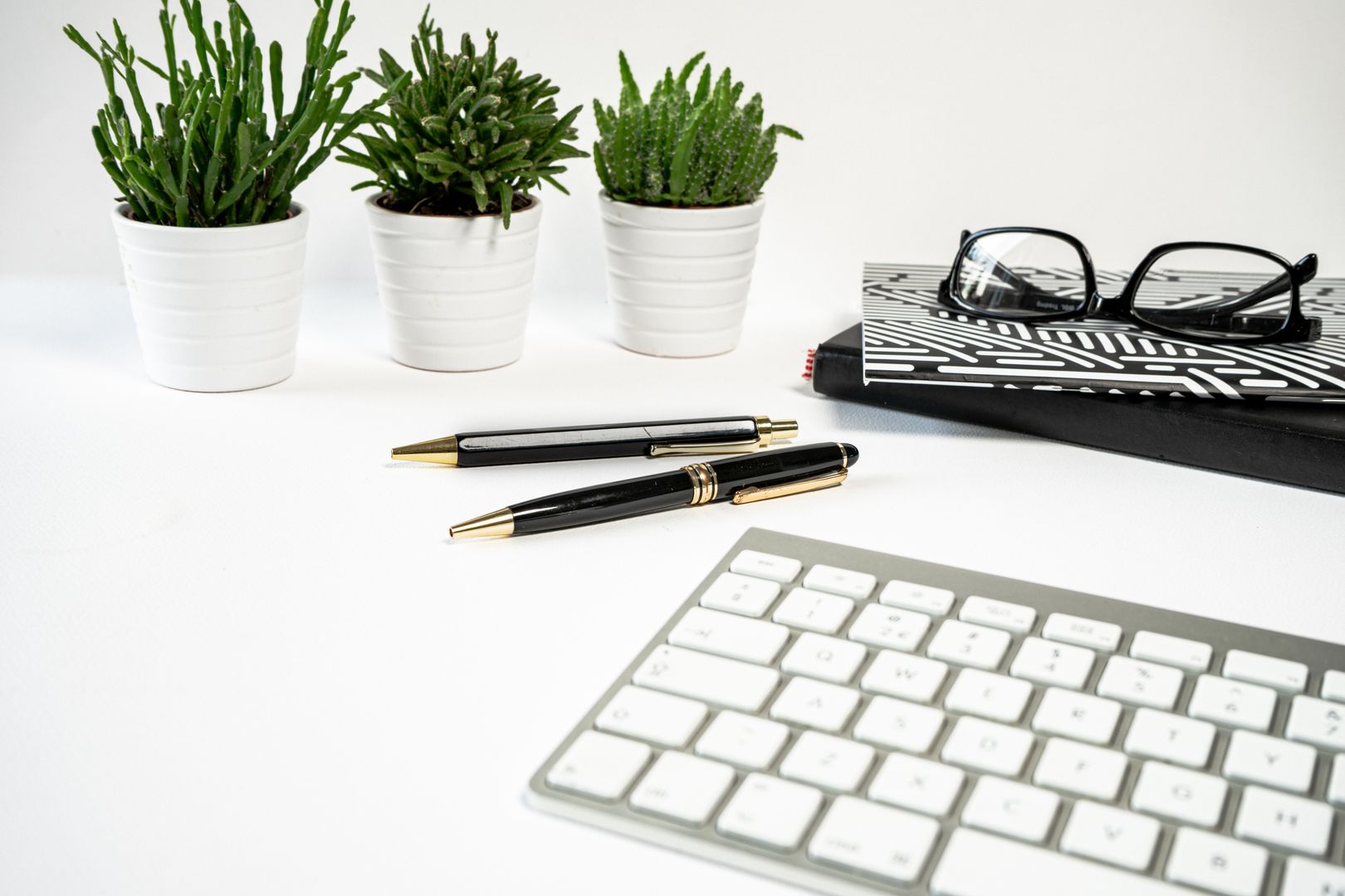 Bright and stylish office desk with keyboard, pens, plants, and notebooks creating a modern workspace vibe.